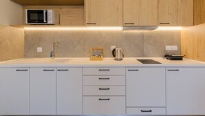 Et moderne køkken med hvide skabe, en stålkedel og en mikrobølgeovn på bordpladen.
