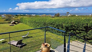 Un balcon donnant sur un vignoble, un espace extérieur aménagé dans un style rustique et une vue lointaine sur la côte.
