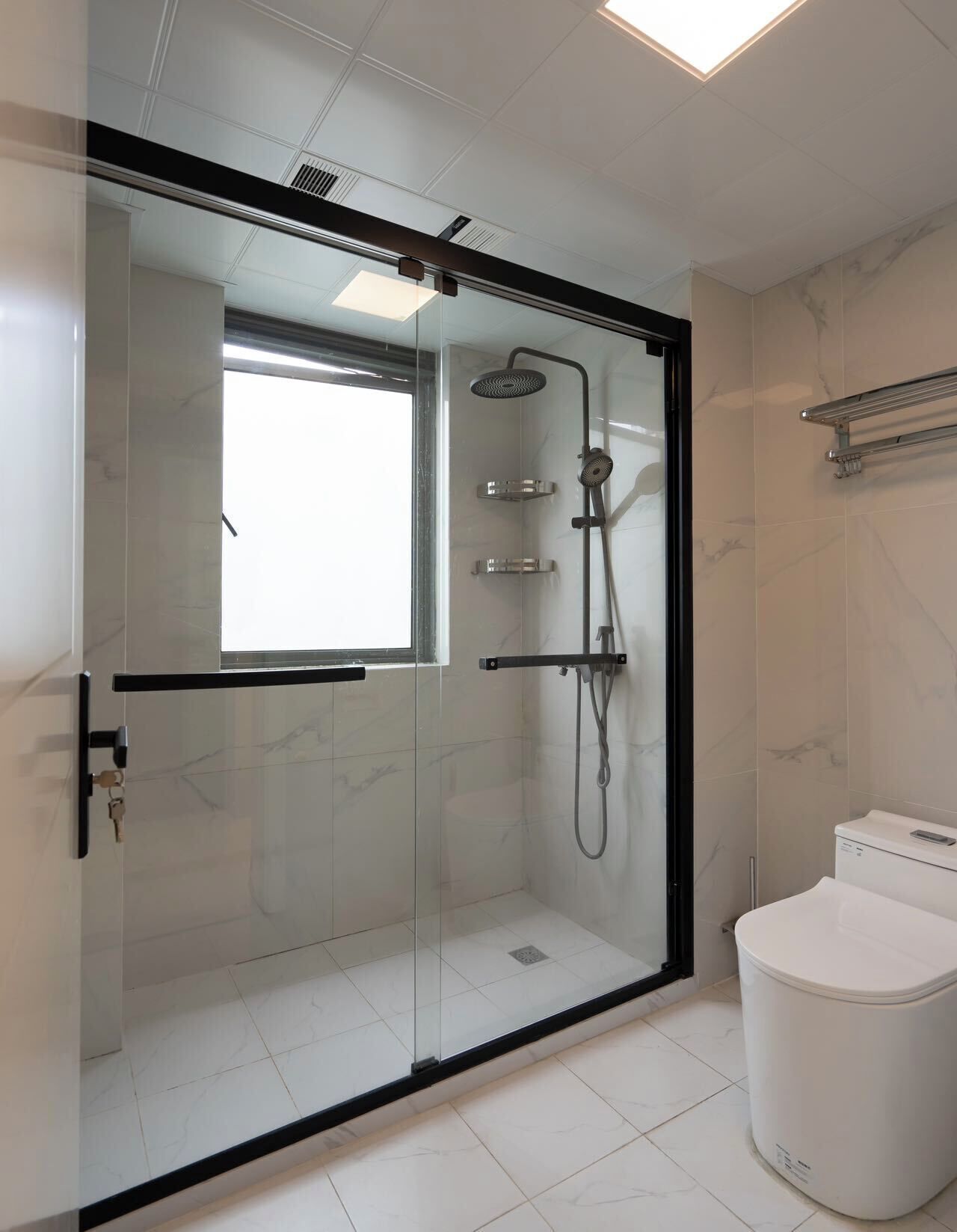 Ein modernes Badezimmer mit einer gläsernen Duschkabine, einer Toilette und einem Boden aus Marmorfliesen.