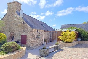 A stone building with a sloped roof, a satellite dish, and potted plants. - Breton Stone Cottage by Sandy Beaches (Landéda)