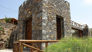 Ein Steinhaus mit einer Holztür und einem Fenster, einem Holzgeländer und einer Steinmauer.