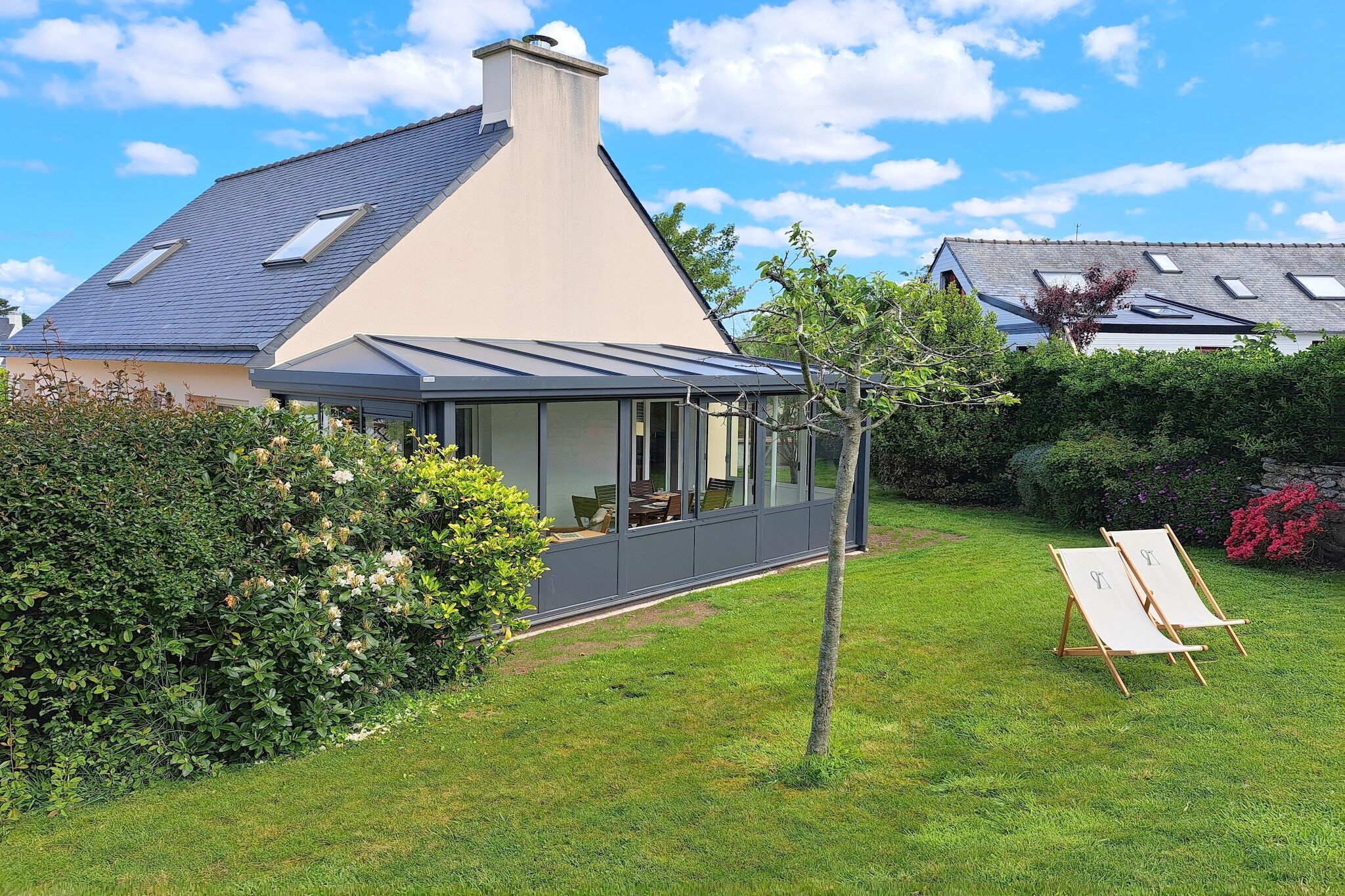 Ein Haus mit einem geneigten Dach, einem Wintergarten und einem gepflegten Rasen.