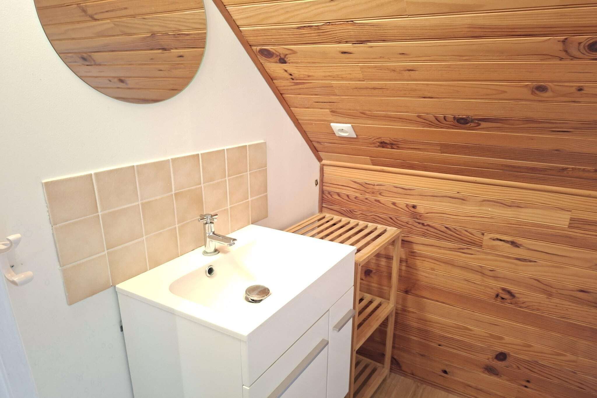 A bathroom with a white sink, a mirror, and wooden paneling.