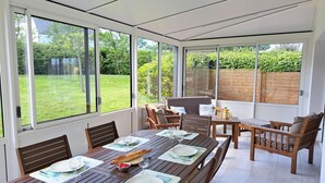 Ein Wintergarten mit einem Esstisch, gedeckt für vier Personen, umgeben von Holzstühlen und einer gepolsterten Bank.