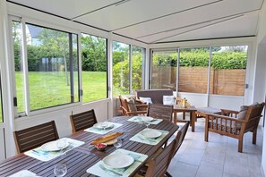 Ein Wintergarten mit einem Esstisch, gedeckt für vier Personen, umgeben von Holzstühlen und einer gepolsterten Bank.