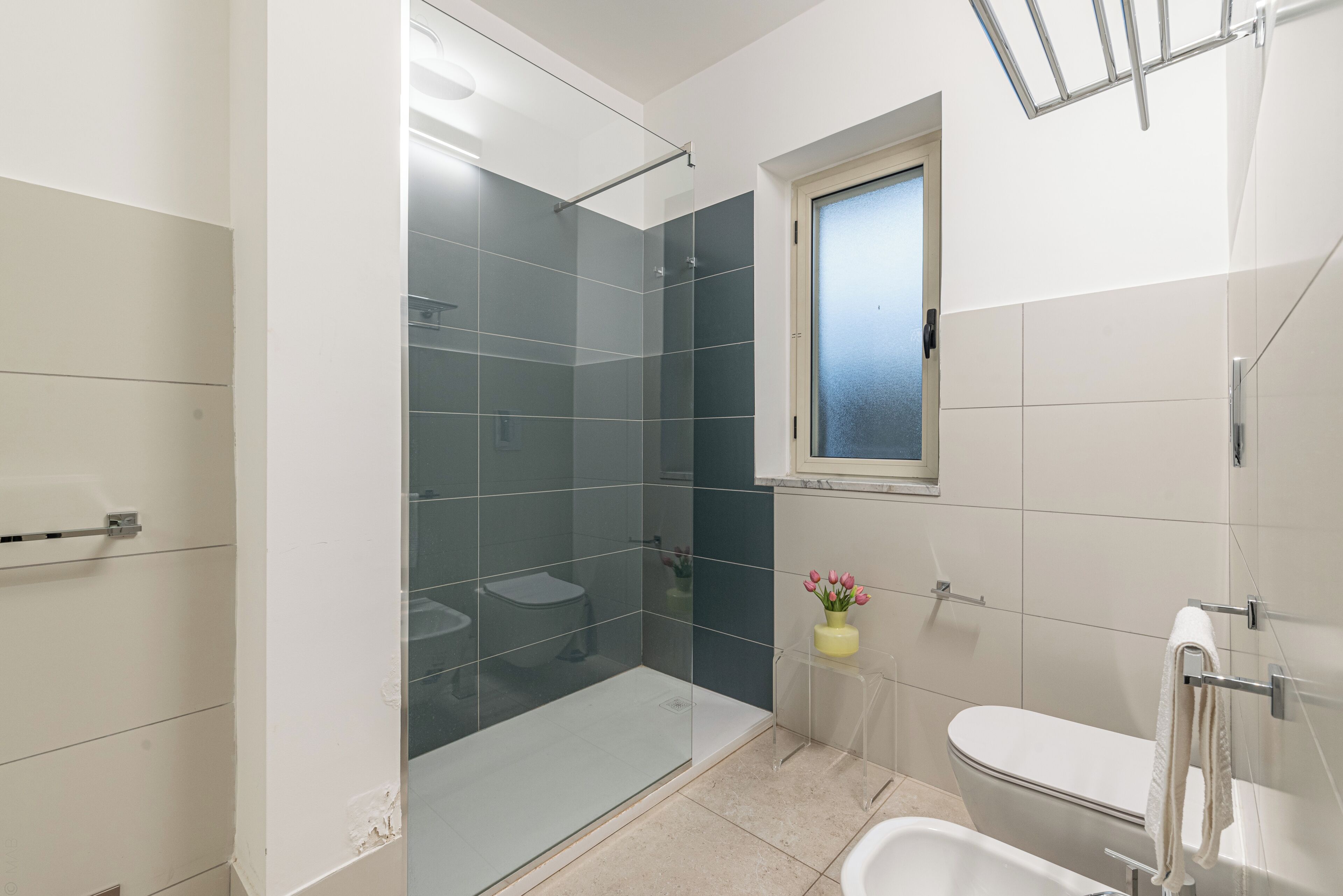 A modern bathroom with a glass-enclosed shower, a toilet, a bathtub, and a window above the toilet.