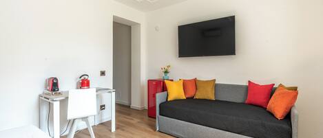 A modern living room with a sofa, a flat-screen TV, a desk, and a red refrigerator.