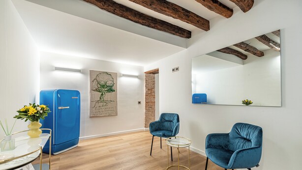 A modern room with a blue refrigerator, two blue chairs, a small round table, and a large mirror on the wall. - Palazzo Ferrara Rooms by Wonderful Italy (Palermo)