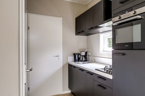 A modern kitchen with dark cabinets, a white countertop, a coffee maker, and a built-in oven. - Lodge 18 | 4 persoons chalet in Zennewijnen (Zennewijnen)