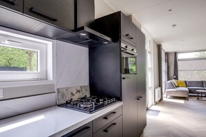 A modern kitchen with a gas stove, integrated oven, and a window overlooking greenery. - Lodge 18 | 4 persoons chalet in Zennewijnen (Zennewijnen)