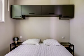 A bedroom with a bed, two bedside tables, a wall-mounted cabinet, and a wall socket. - Lodge 18 | 4 persoons chalet in Zennewijnen (Zennewijnen)