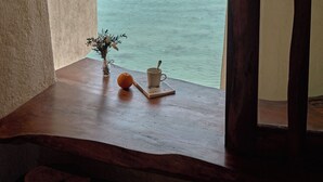 A view through a window with a wooden frame, a small table with a vase and a cup, and a distant island. - Ibala Hotel & Spa (Bac Nha Trang)