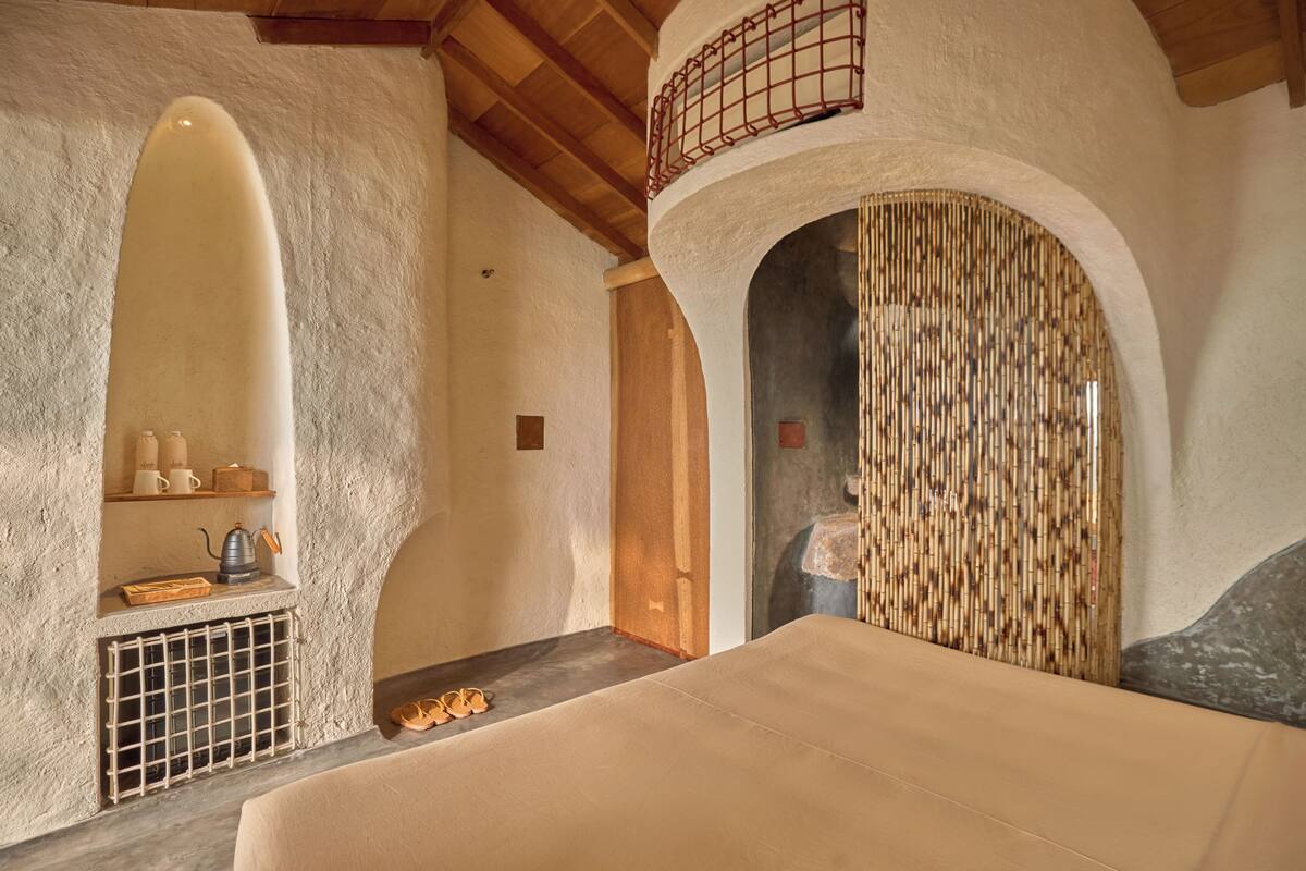 A room with a bed, a shelf with cups and a kettle, and a door leading to another room.