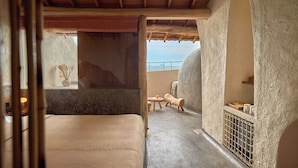 A room with a bed, a small table, a chair, a wooden bench, and a view of the sky. - Ibala Hotel & Spa (Bac Nha Trang)