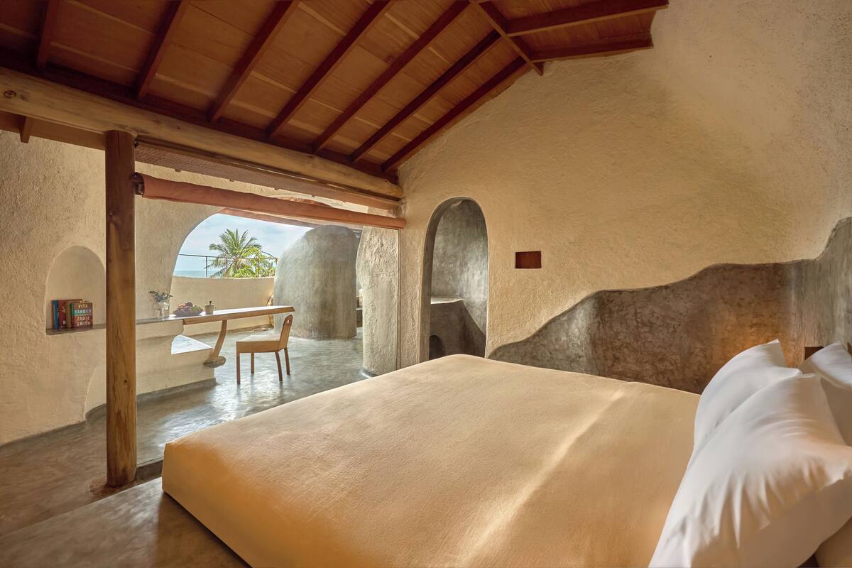 A bedroom with a large bed, a wooden table, and a view of palm trees.