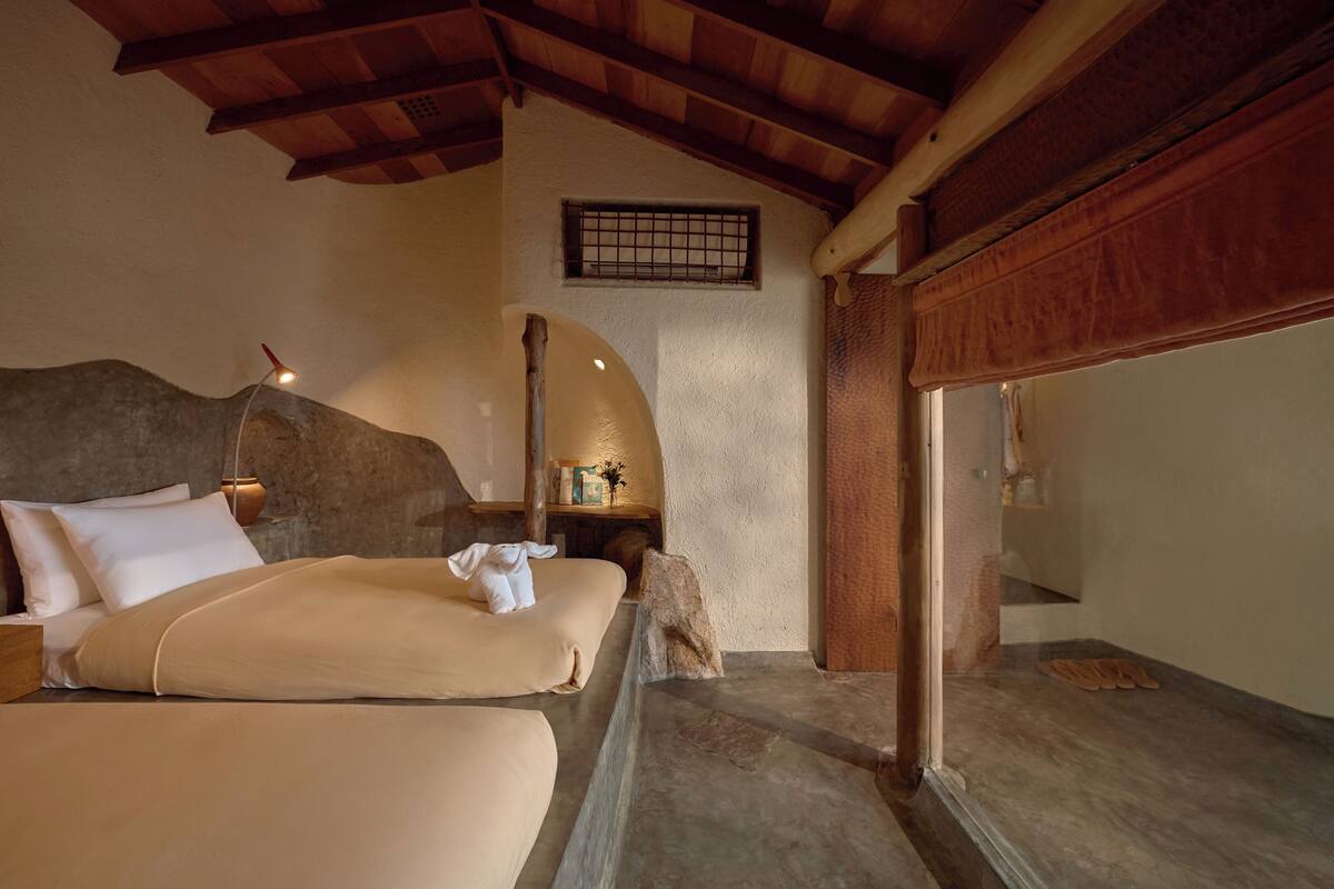 A bedroom with a bed, a nightstand, a window, and a wooden ceiling.