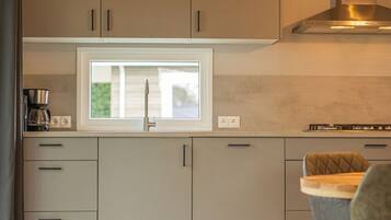 Une cuisine moderne avec des meubles gris, une fenêtre, une cuisinière encastrée et un coin repas avec une chaise.