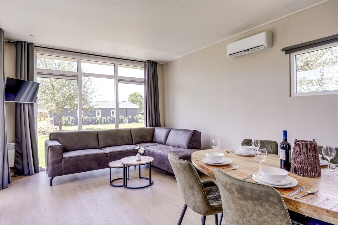 Una sala moderna con un sofá, una mesa de comedor para dos personas y un televisor montado en la pared.