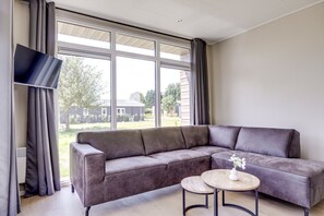 Un salon moderne avec un canapé d’angle, une petite table ronde et un téléviseur à écran plat.