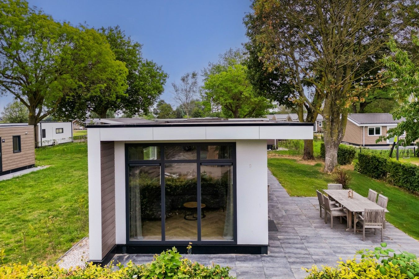 A modern outdoor patio area with a dining table and chairs, surrounded by a well-maintained lawn and trees.