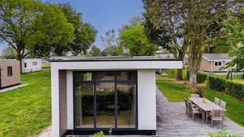 A modern outdoor patio area with a dining table and chairs, surrounded by a well-maintained lawn and trees.