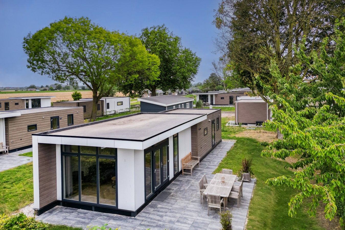 Een moderne stacaravan met een plat dak, grote ramen en een terras met tuinmeubilair.