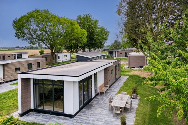 A modern mobile home with a flat roof, large windows, and a patio with outdoor furniture.