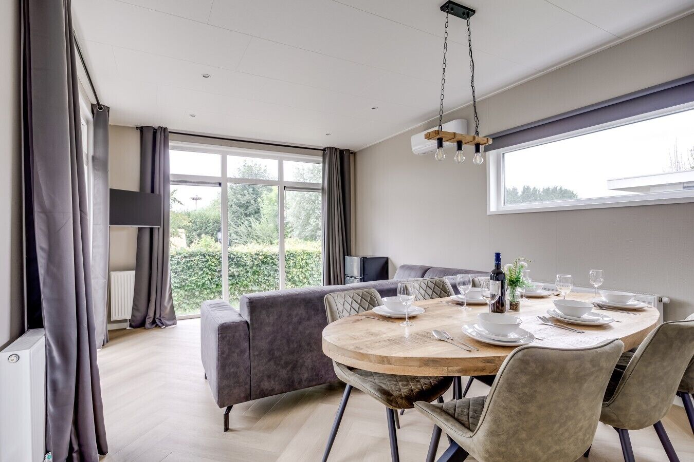 Un coin repas avec une table ronde dressée pour quatre personnes, un canapé et une vue sur la verdure à l’extérieur.