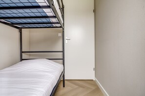 Una cama litera con tragaluz, una pared blanca y un suelo de madera.