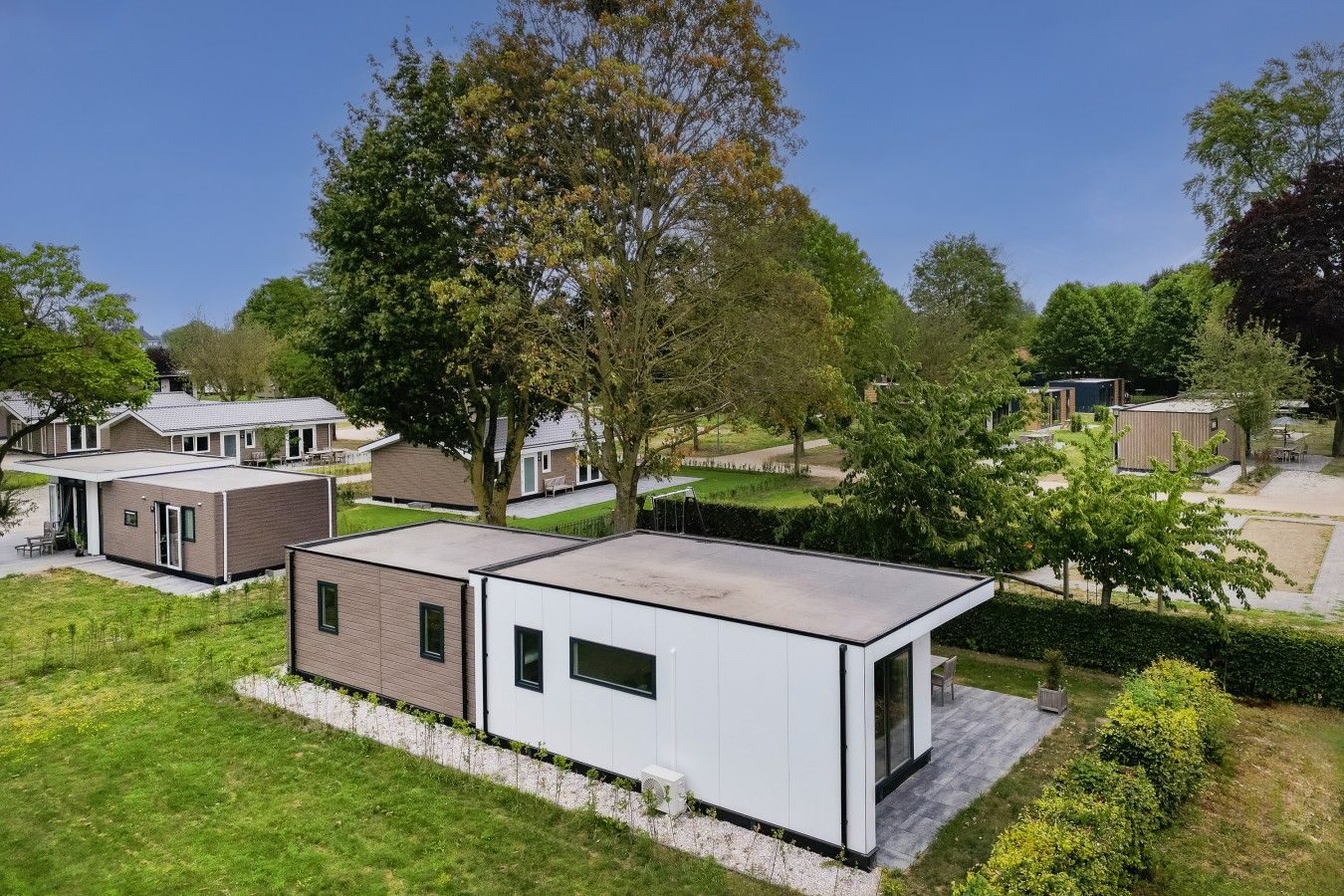 A modern residential area with detached houses, a flat roofed structure, and a well-maintained lawn.