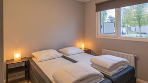 Ein Schlafzimmer mit Doppelbett, Nachttischen, einem Fenster und einer Heizung.
