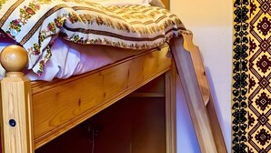 Un lit superposé avec une couvre-lit à motifs, une tête de lit en bois et un luminaire fixé au mur.