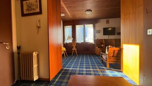 Une pièce avec un sol à carreaux, une porte en bois, un radiateur, une chaise et un téléviseur.