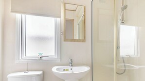 A bathroom with a toilet, sink, mirror, and shower. - Gold 3 Bedroom Caravan, Sleeps 8. With parking. (Great Yarmouth)