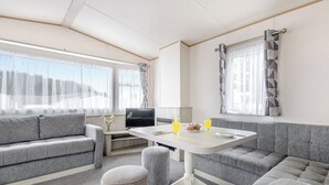 A modern RV interior with a sofa, table, ottoman, and a TV. - Gold 3 Bedroom Caravan, Sleeps 8. With parking. (Great Yarmouth)