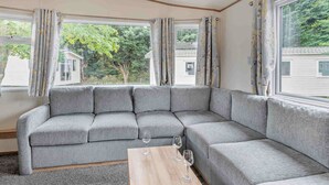 Un salón con zona de descanso, un sofá modular gris, una mesa de centro de madera y ventanas amplias con cortinas.
