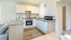 Una cucina compatta con mobili bianchi, forno integrato, microonde e un'area pranzo con tavolo e sedie in legno.