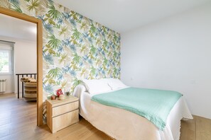 Une chambre à coucher avec un lit, une table de chevet en bois, un miroir et un mur décoré d’un motif de feuilles tropicales.