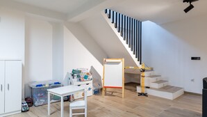 Una habitación con una escalera, una mesa blanca y un contenedor de plástico.