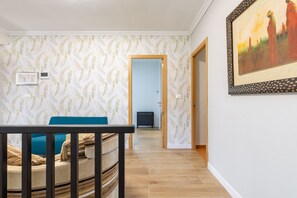 Une pièce avec un papier peint à motifs, un plancher en bois, une table à manger avec un coussin bleu et un tableau accroché au mur.