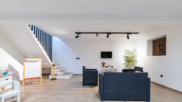 Amplia sala de estar con escalera, televisor de pantalla plana, sofá y mesa de comedor.
