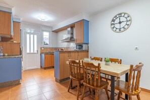 Une cuisine avec des meubles de rangement en bois, un four à micro-ondes, une horloge et une table à manger avec des chaises.