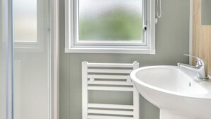 Een badkamer met een witte wasbak, een handdoekhouder en een matig doorschijnend raam.