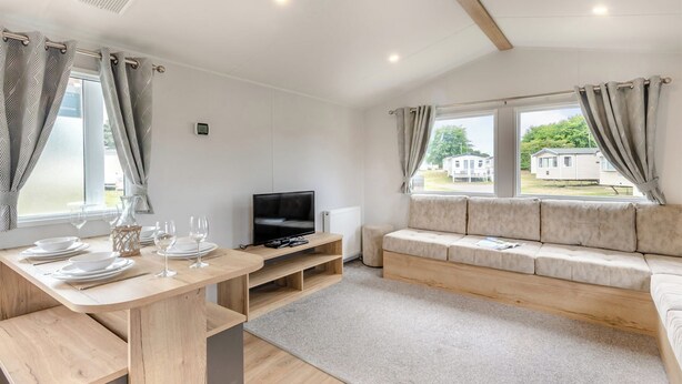 Een moderne woonkamer met een houten eettafel, bank, televisie en grote ramen.