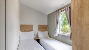 Een kleine, schone kamer met twee bedden, een raam met gordijnen, en een houten hoofdbord.
