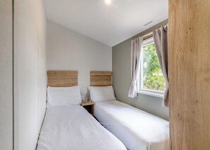 Ein kleines, sauberes Zimmer mit zwei Betten, einem Fenster mit Vorhängen und einem hölzernen Kopfteil.
