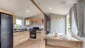 Een moderne keuken met houten kastjes, een zwarte koelkast, een magnetron, een fornuis en een eethoek met een tafel voor twee personen.