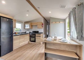 Eine moderne Küche mit Holzausstattung, einem schwarzen Kühlschrank, einer Mikrowelle, einem Herd und einer Essecke mit Tisch für zwei Personen.