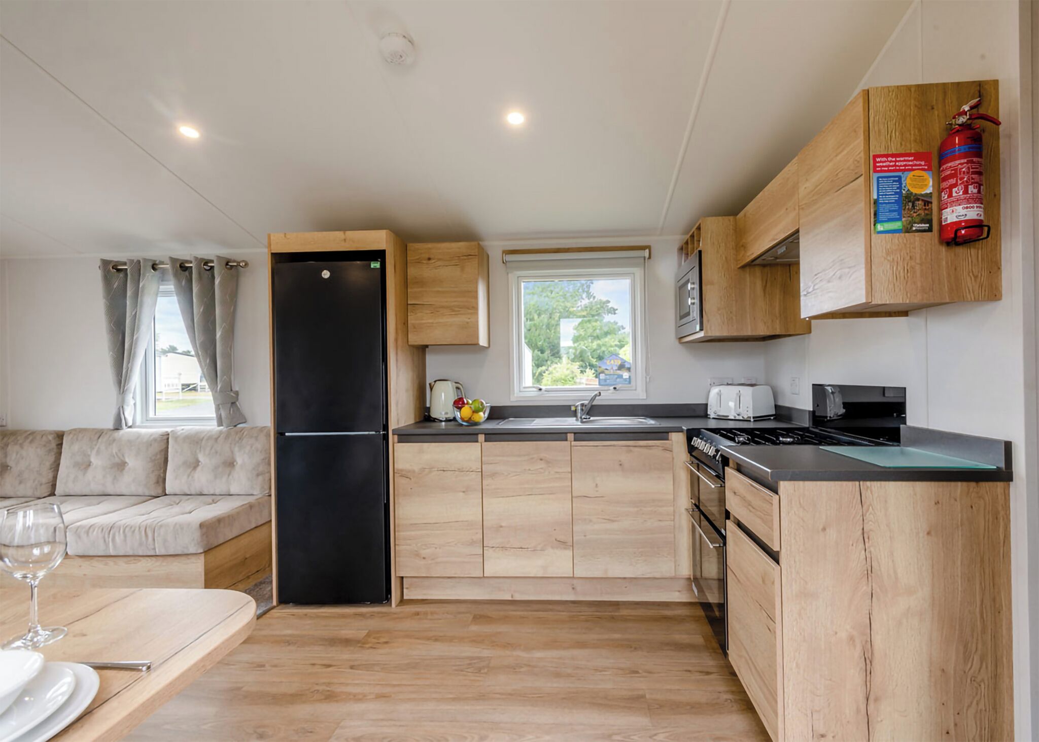 A compact kitchen with wooden cabinets, a black refrigerator, a stove, and a window with a view of greenery.