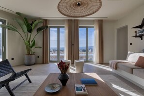 A modern living room with a large potted plant, a black woven chair, a wooden coffee table, and a sofa with a view through large windows. - Villa Calisto – A Sunset Sanctuary (2524+VXR Paros, Greece)